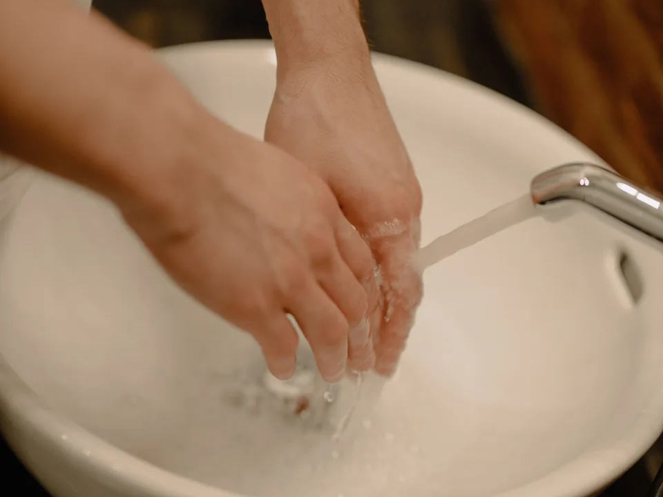 Hands rinsed under running water over a light ceramic basin.